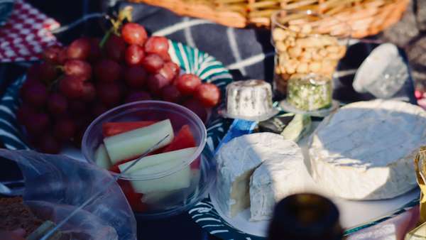 Närbild på en picnic uppdukat på en mörkblå filt. Ostar, vindruvor och uppskurna meloner är tydliga.