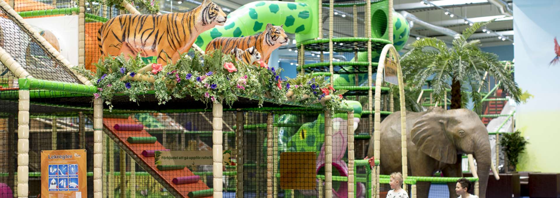 Två små pojkar springer och leker på Leos Lekland. På bilden syns stora färgglada klätterställningar och två tigrar och en stor elefant i plast.