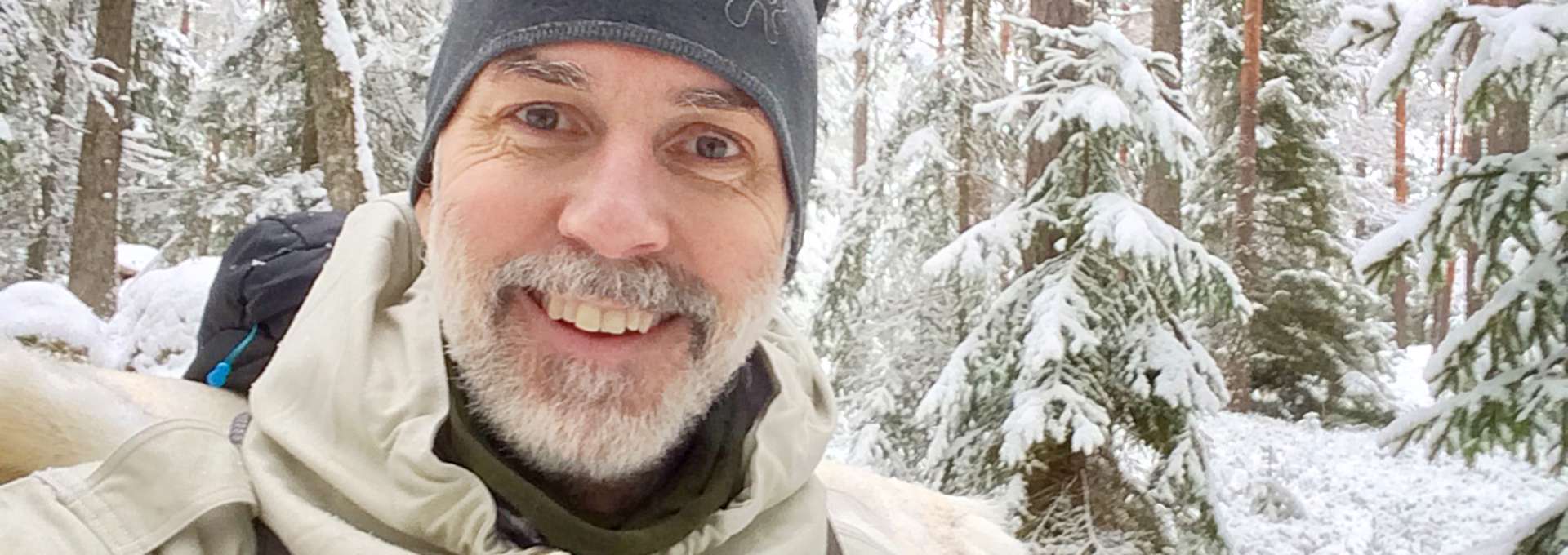 En selfie på en leende man i en snöig granskog. 