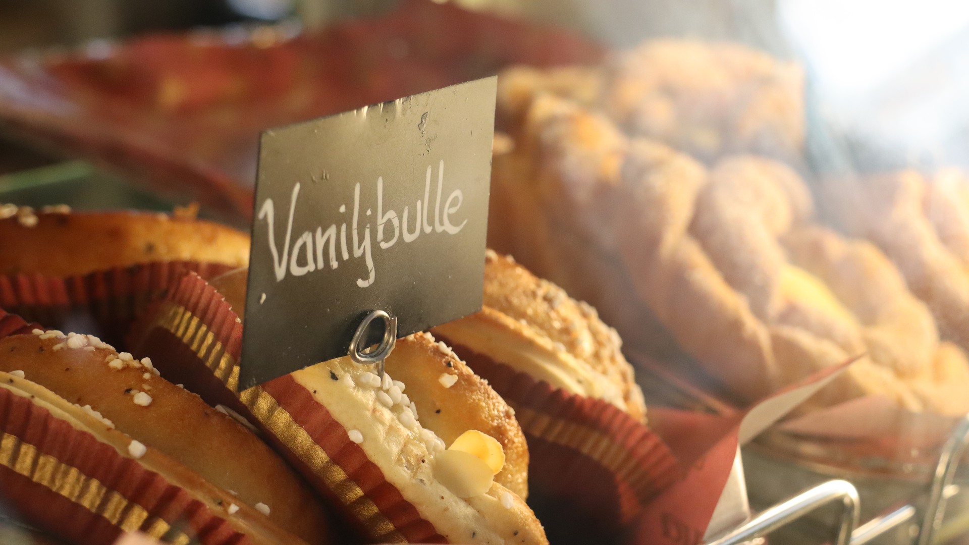 Some buns behind a glass counter and a sign that says Vaniljbulle (vanilla bun)